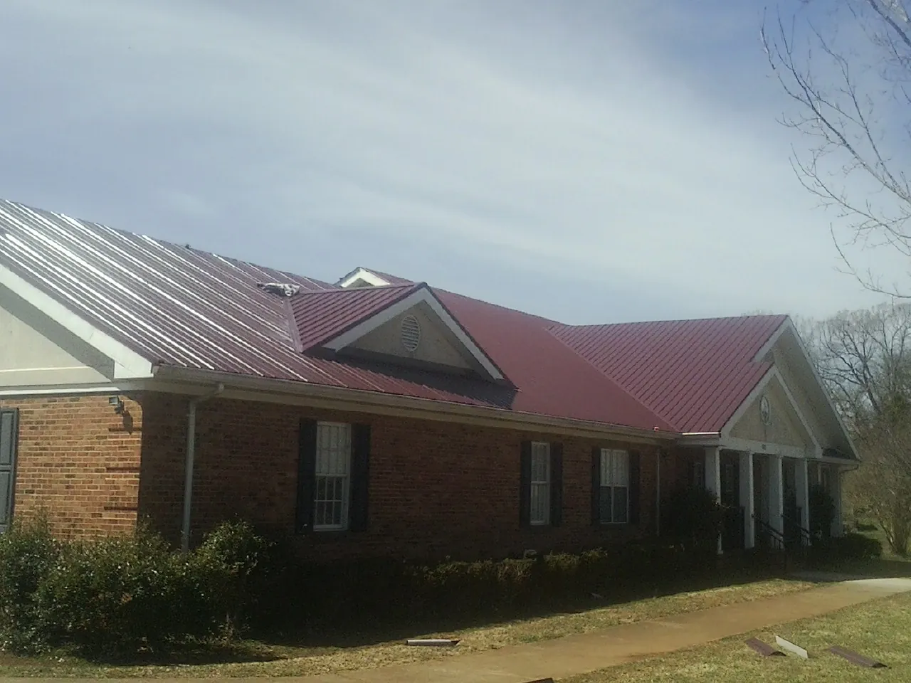 Red metal roof with gabled entries on a long brick building, from a Hail Damage Roof Repair job in Norwalk